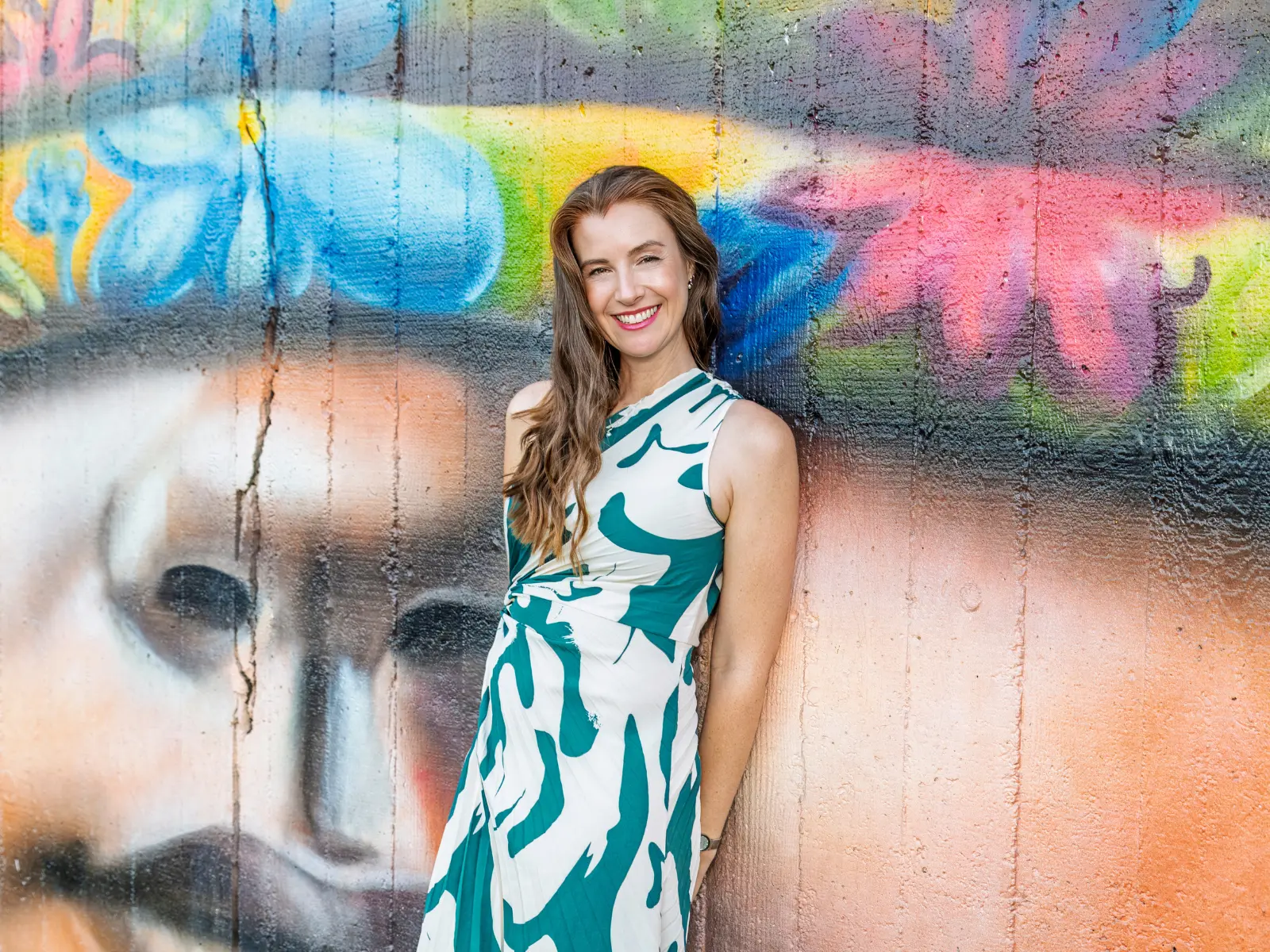 Sarah Rus, Relationship and Leadership Coach, smiling against a colourful Melbourne street-art wall