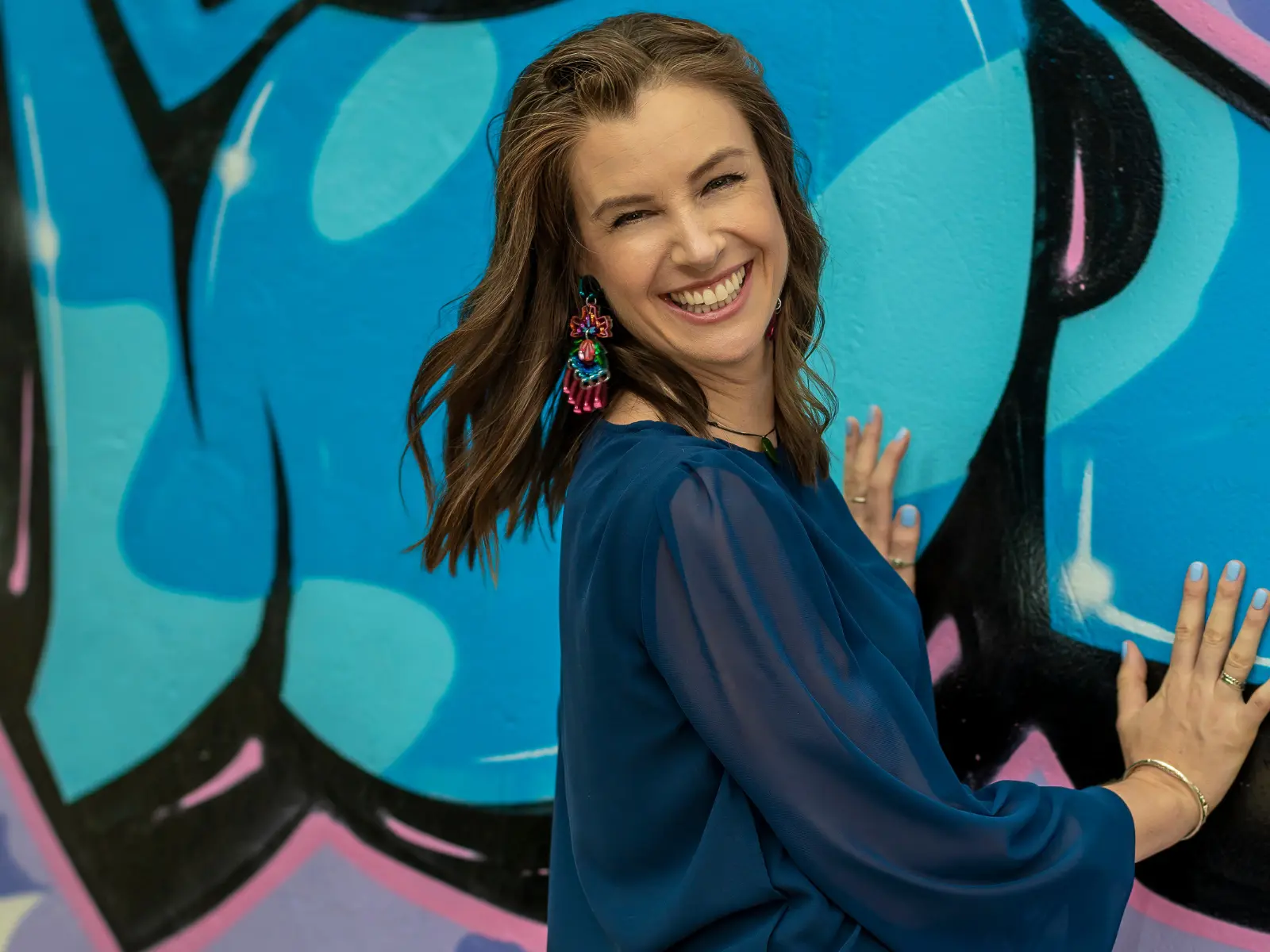 Sarah Rus, Relationship and Leadership Coach, laughing against a blue street-art wall